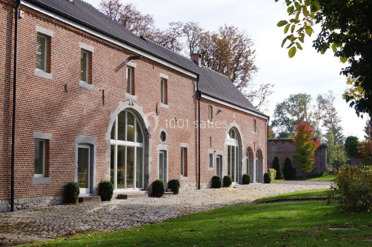 Bâtiment en briques rouges avec grandes fenêtres cintrées, entouré de verdure et d'une allée pavée.
