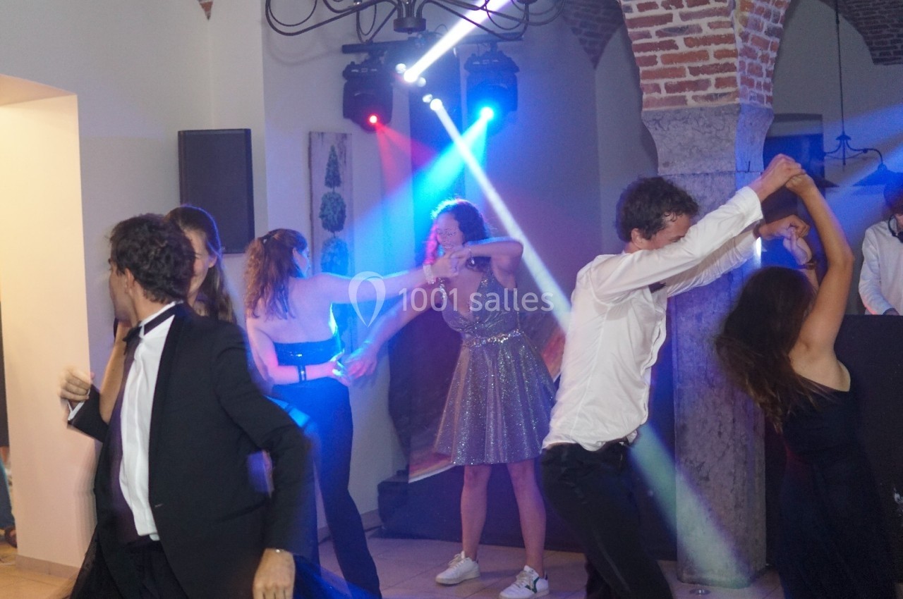 Des personnes dansent sous des lumières colorées dans une salle avec des murs en briques et des arches en pierre.