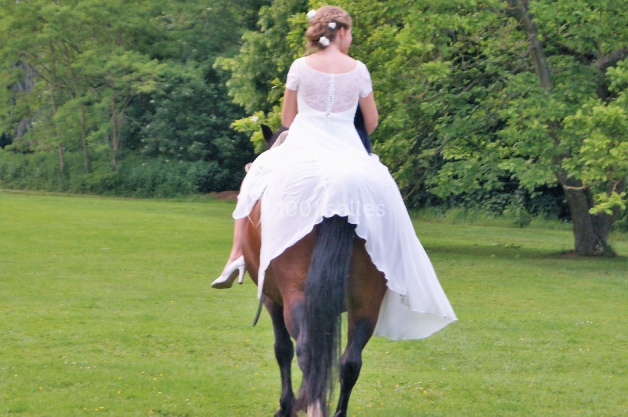 Une femme en robe blanche monte un cheval brun dans un parc verdoyant.