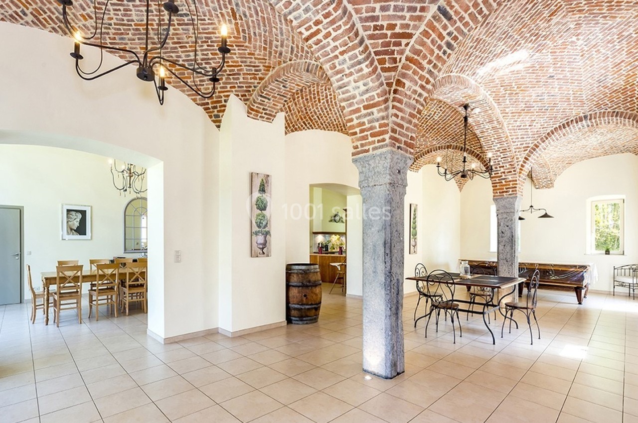 Salle lumineuse avec voûtes en briques, tables et chaises en bois et métal, décorée de tableaux et d'un tonneau.