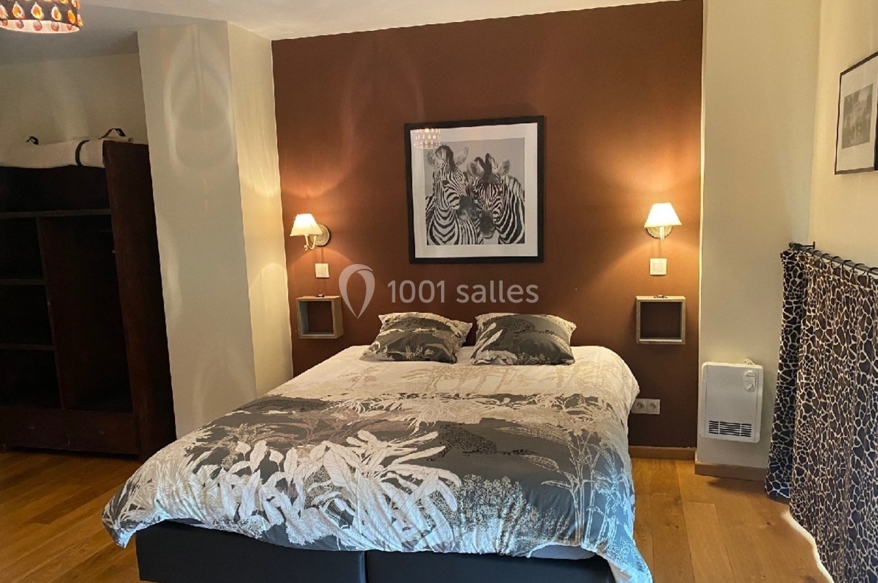 Lit double avec housse à motifs végétaux, encadré par deux appliques murales, dans une chambre au mur brun décoré.