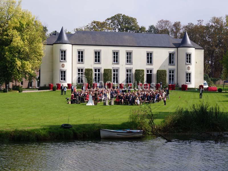 Groupe de personnes rassemblées devant un château blanc avec tours, entouré de pelouses et d'un plan d'eau au premier plan.