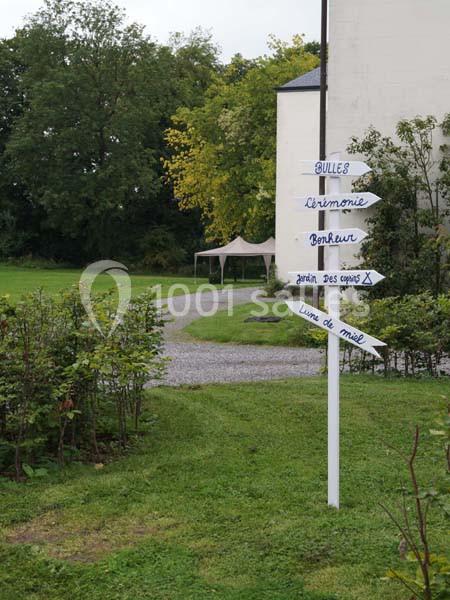 Panneau directionnel en bois dans un jardin, indiquant divers lieux comme ’cérémonie’ et ’livre d'or’.