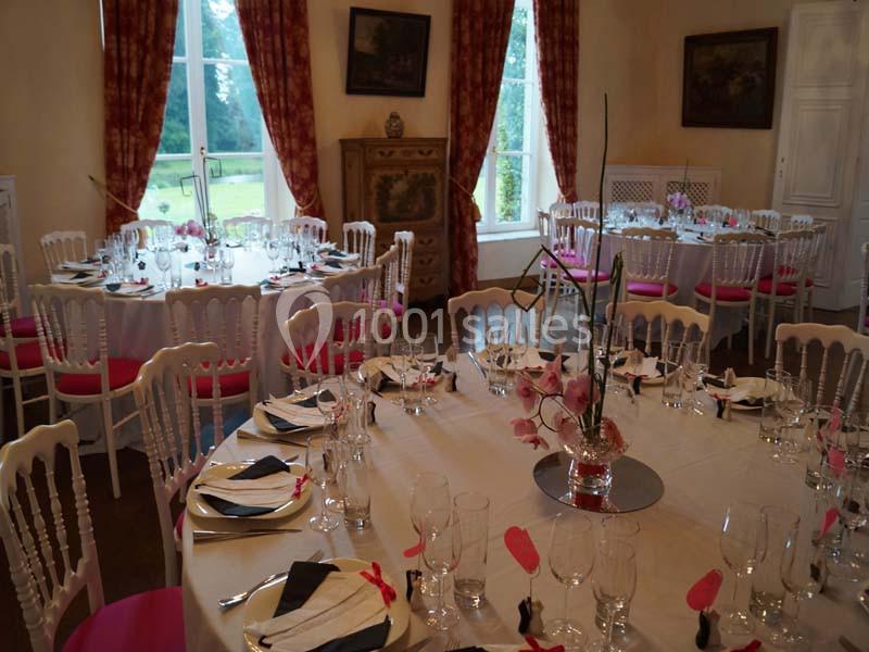 Salle de réception élégamment dressée avec des tables rondes, nappes blanches, chaises décorées et centre de table floral.