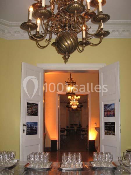 Vue d'une salle élégante avec lustres, portes ouvertes et table dressée de verres sur des plateaux.