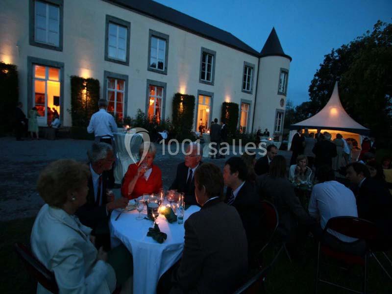 Groupe de personnes dînant en soirée dans le jardin éclairé d'un bâtiment de style château.