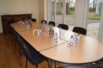 Salle de réunion avec une grande table en bois, chaises noires, bouteilles d'eau et vue sur l'extérieur par des baies…