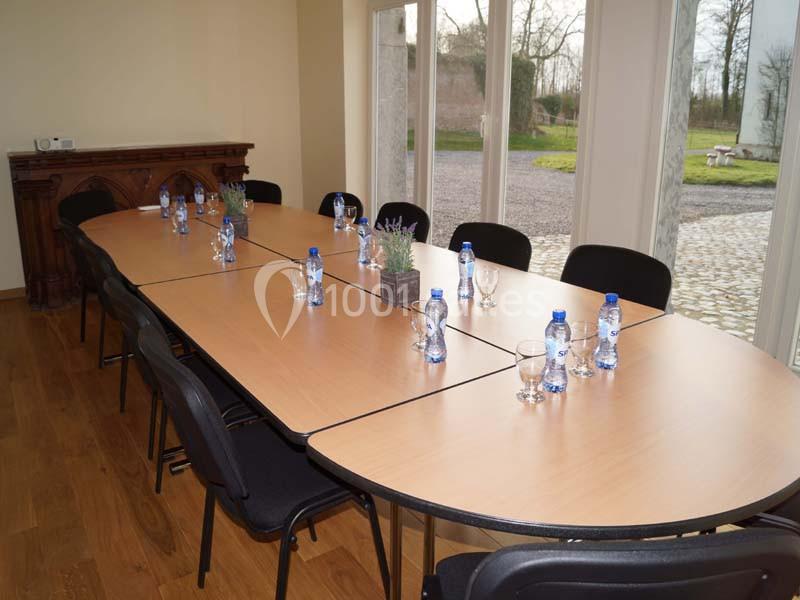 Salle de réunion avec une grande table en bois, chaises noires, bouteilles d'eau et vue sur l'extérieur par des baies…
