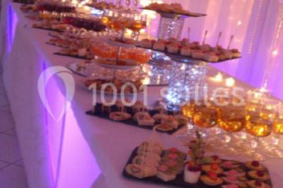 Salle de réception décorée avec des lumières roses et un éclairage scintillant, tables dressées et plafond drapé.