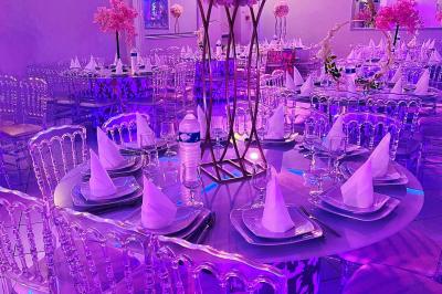 Salle de réception décorée avec des lumières roses et un éclairage scintillant, tables dressées et plafond drapé.
