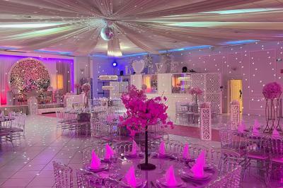 Salle de réception décorée avec des lumières roses et un éclairage scintillant, tables dressées et plafond drapé.