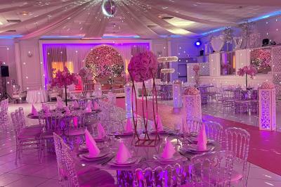 Salle de réception décorée avec des lumières roses et un éclairage scintillant, tables dressées et plafond drapé.