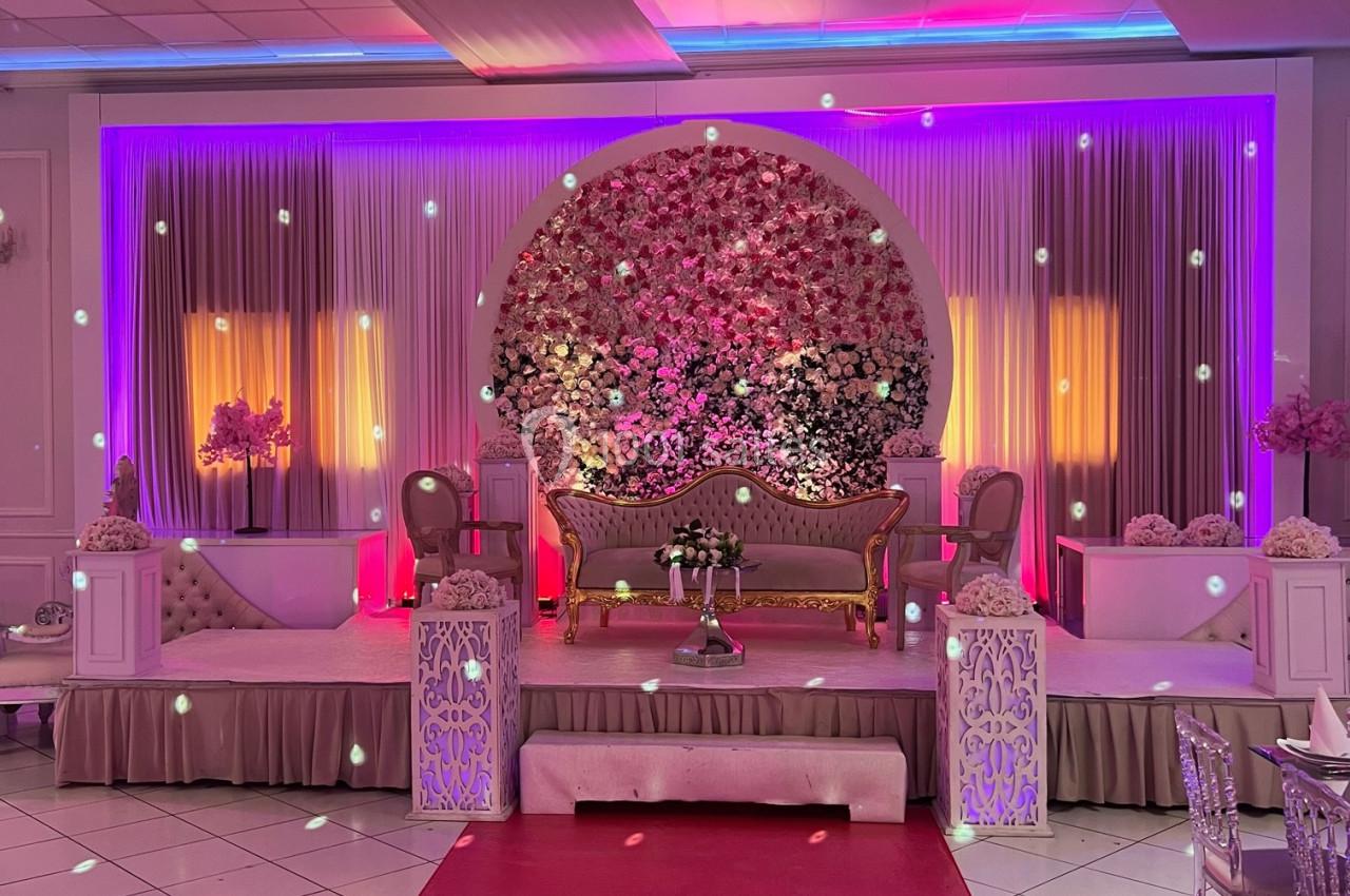 Décor de scène de mariage avec canapé central, murs ornés de fleurs et éclairage coloré dans une salle de réception.