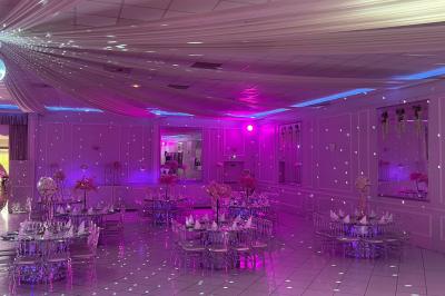 Salle de réception décorée avec des lumières roses et un éclairage scintillant, tables dressées et plafond drapé.