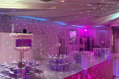 Salle de réception décorée avec des lumières roses et un éclairage scintillant, tables dressées et plafond drapé.