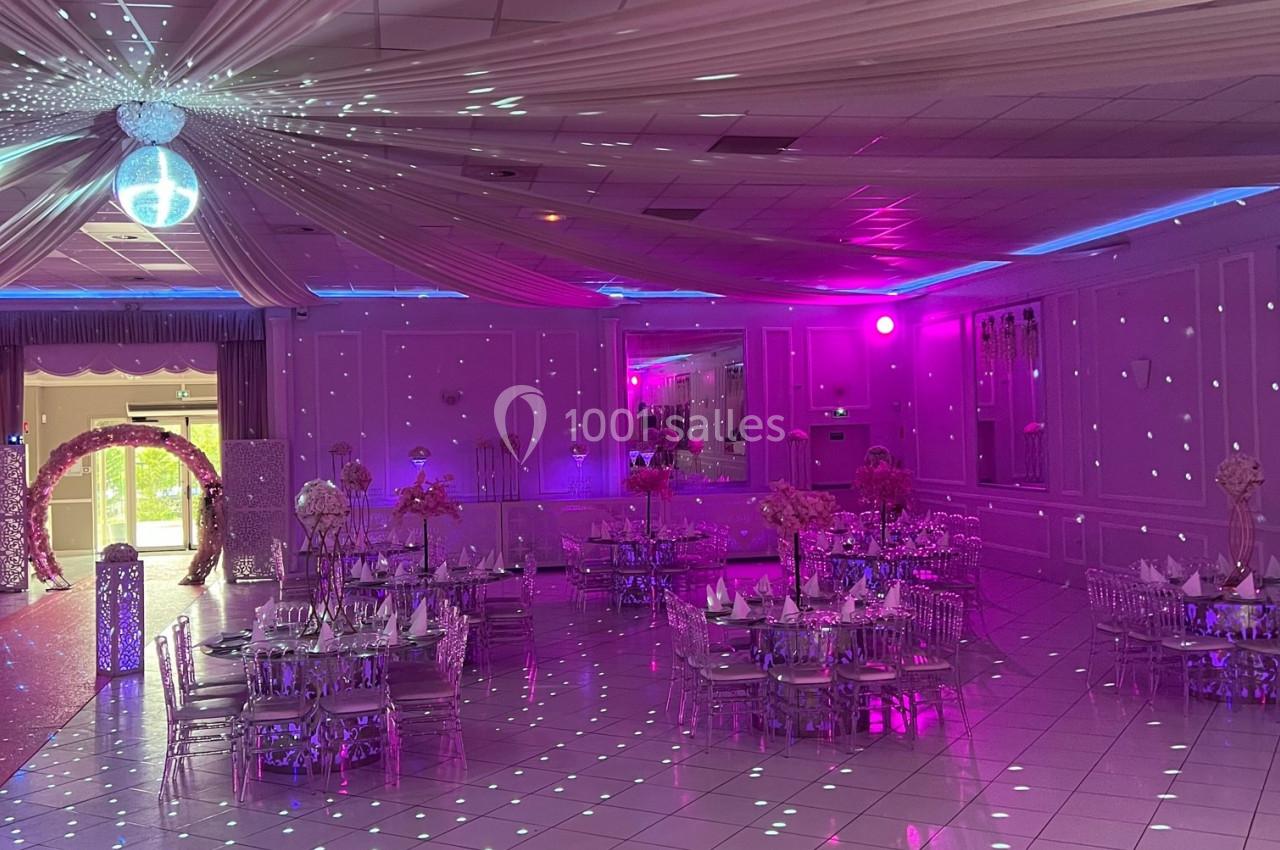 Salle de réception décorée avec des tables dressées, éclairage rose et jeux de lumière sur le sol et le plafond.