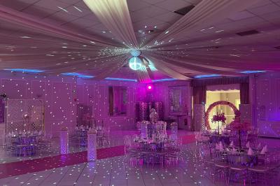 Salle de réception décorée avec des lumières roses et un éclairage scintillant, tables dressées et plafond drapé.