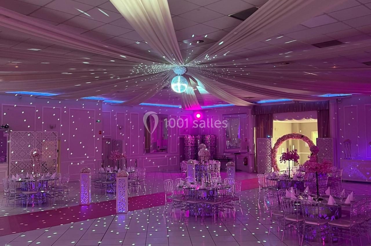 Salle de réception décorée avec des drapés au plafond, éclairage violet et tables dressées pour un événement.