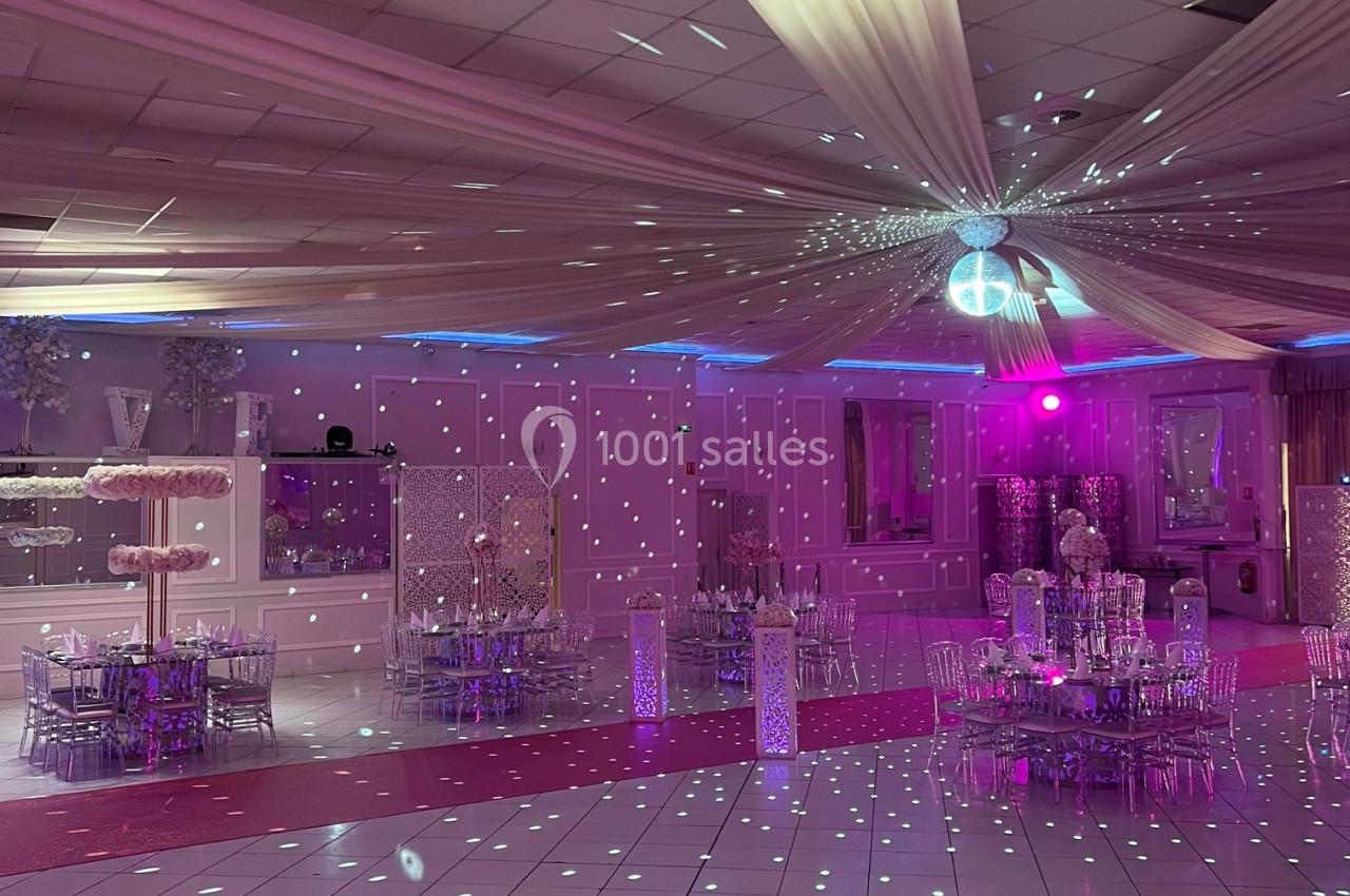 Salle de réception décorée avec des lumières roses et un éclairage scintillant, tables dressées et plafond drapé.