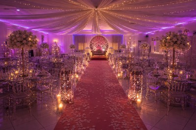 Salle de réception décorée avec des lumières tamisées, des fleurs blanches et des tables élégantes sous un plafond illuminé.