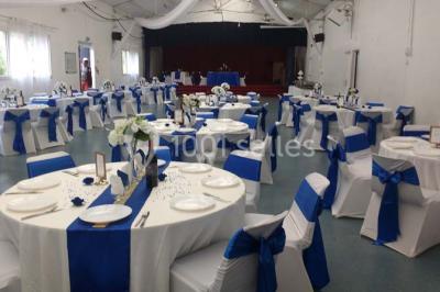 Salle de réception avec des chaises blanches décorées de nœuds, disposées autour de tables sur un sol en parquet clair.