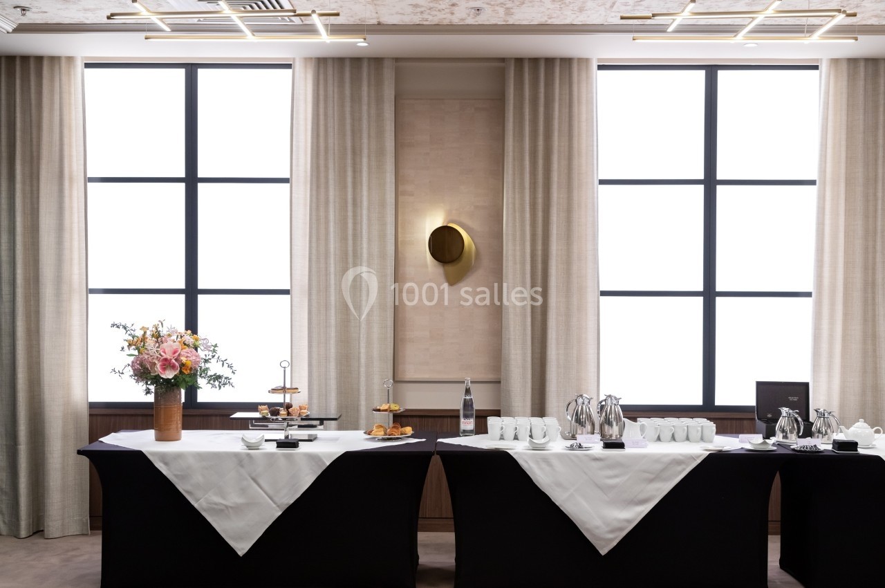 Tables dressées avec nappes noires et blanches, disposant de boissons, tasses, viennoiseries et fleurs en décoration.