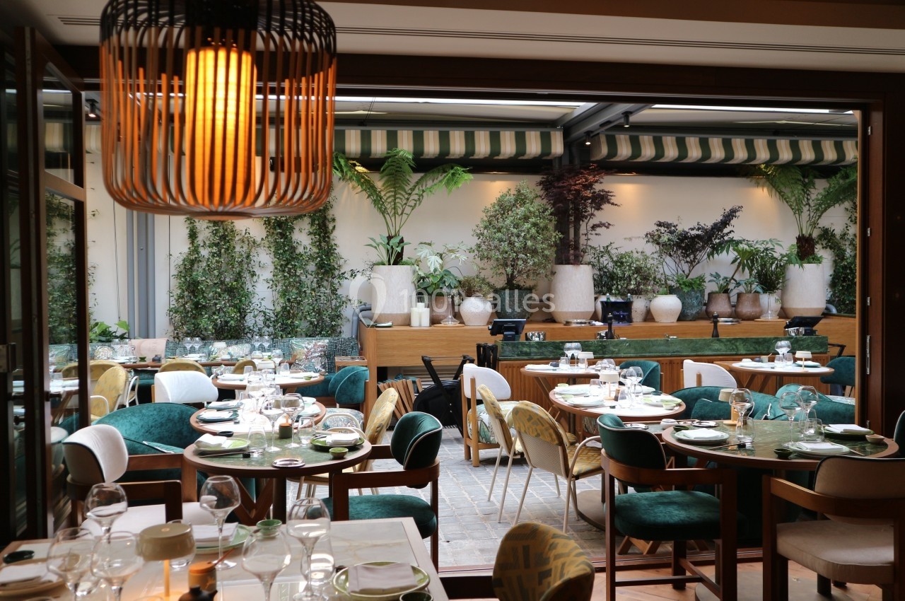 Salle de restaurant élégante avec tables dressées, chaises colorées et terrasse végétalisée en arrière-plan.