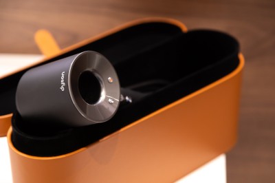 Sèche-cheveux noir dans un étui rigide ouvert de couleur marron, posé sur une surface claire.