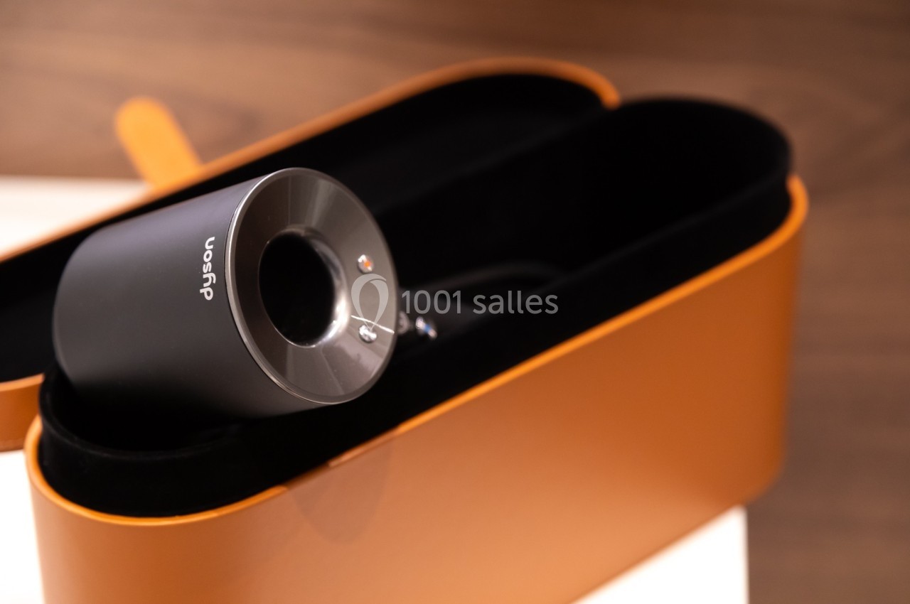 Sèche-cheveux noir dans un étui rigide ouvert de couleur marron, posé sur une surface claire.