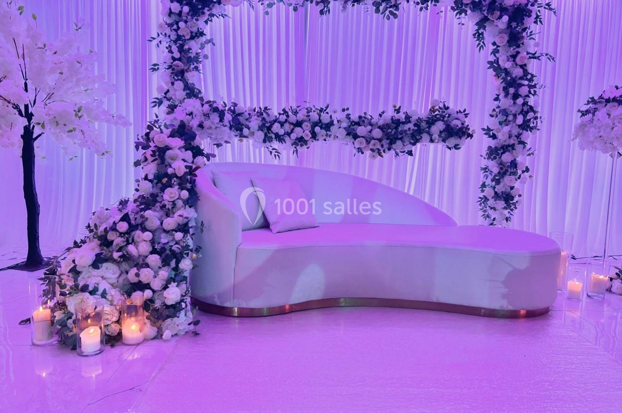 Canapé blanc entouré de fleurs blanches et violettes, avec des bougies allumées sur un sol brillant.