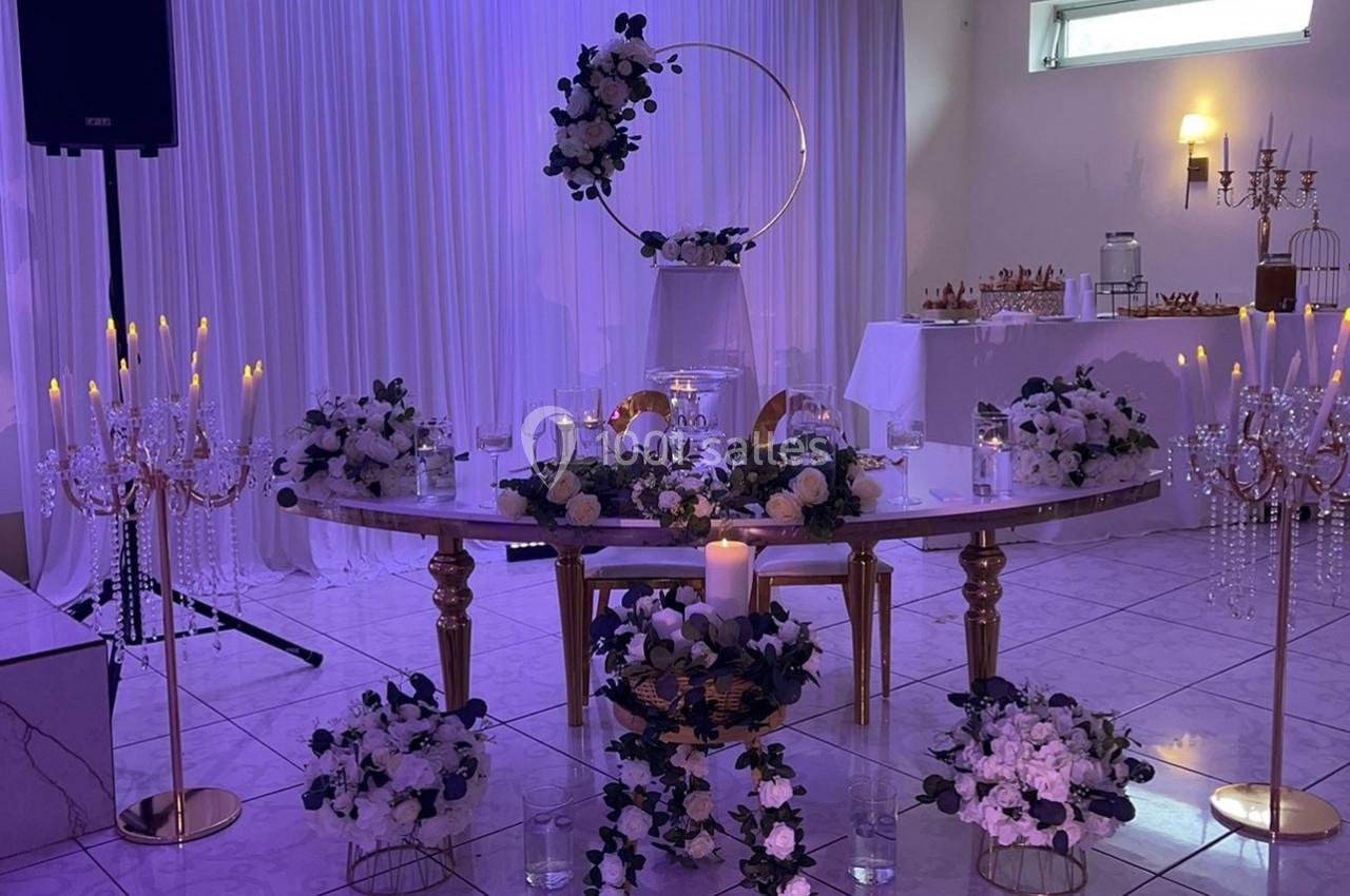 Table décorée pour un événement avec fleurs blanches et violettes, chandeliers dorés et éclairage violet en arrière-plan.