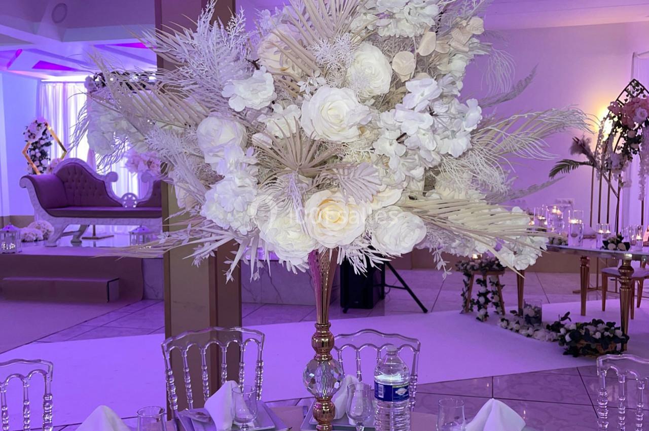 Centre de table élégant avec des fleurs blanches et des feuillages, sur une table dressée dans une salle de réception.