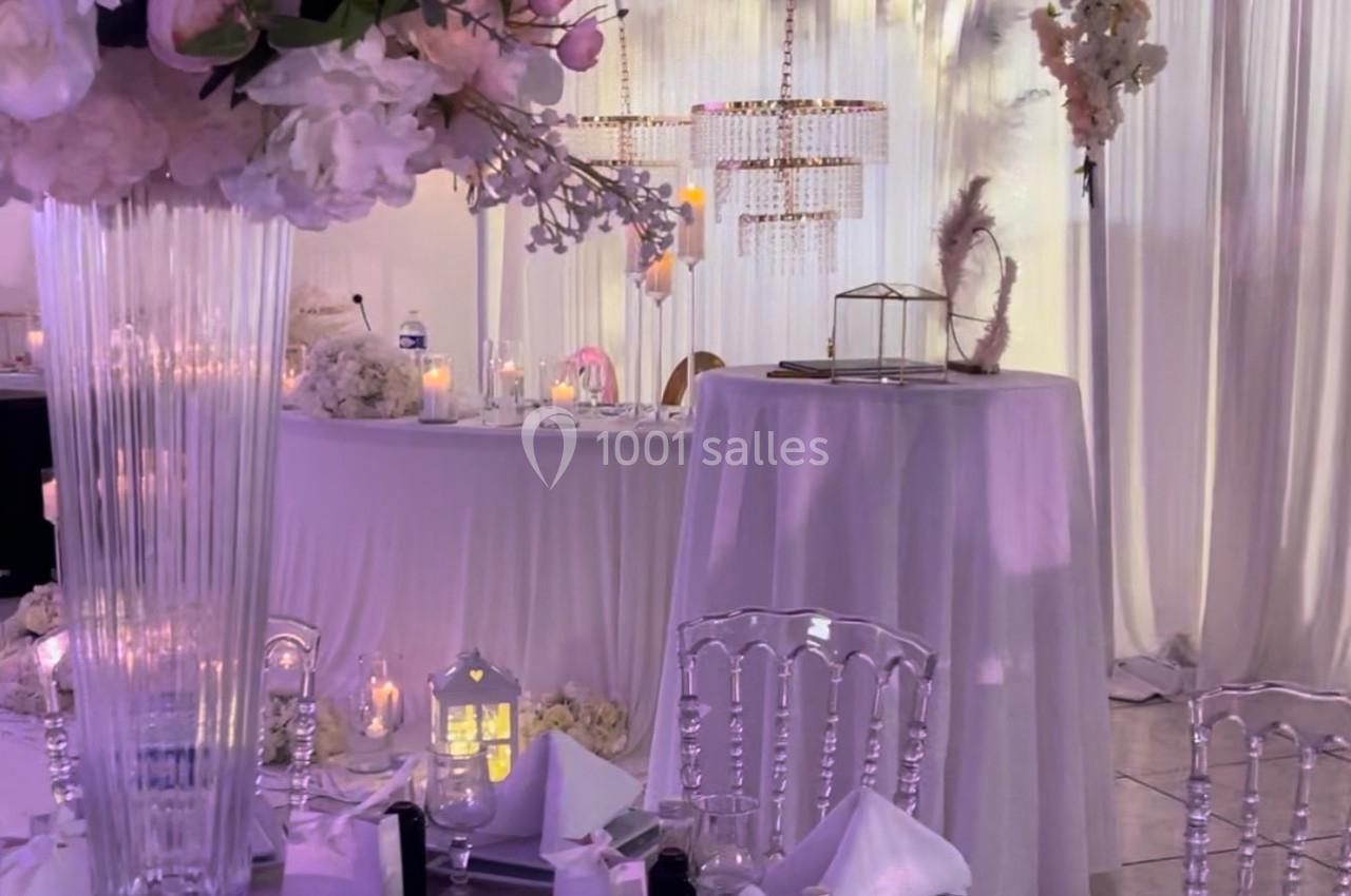 Salle de réception décorée avec des tables élégantes, des fleurs, des chandeliers et un éclairage doux.