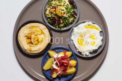 Assiette ronde contenant du houmous, une salade, des pommes de terre rôties et un plat à base de yaourt.