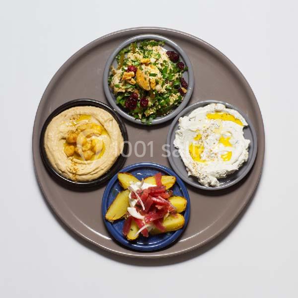 Assiette ronde contenant du houmous, une salade, des pommes de terre rôties et un plat à base de yaourt.