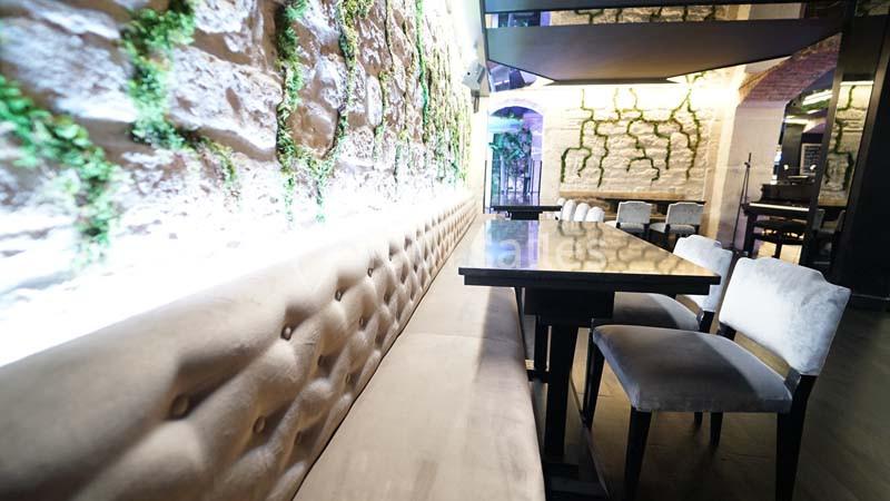 Banquettes et chaises alignées autour de tables dans un intérieur moderne avec murs en pierre et touches de verdure.