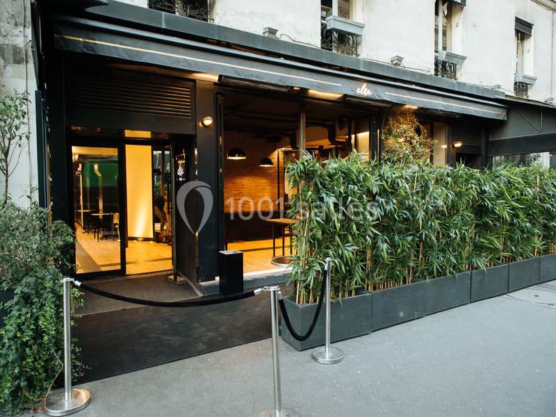 Façade d'un restaurant moderne avec terrasse végétalisée, grandes baies vitrées et entrée délimitée par une corde.