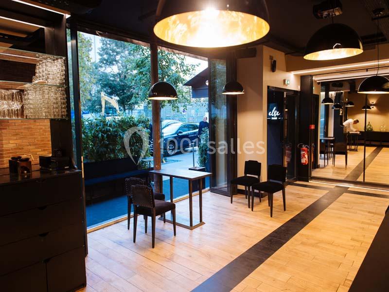 Intérieur d'un espace moderne avec parquet, grandes baies vitrées, mobilier noir et vue sur l'extérieur arboré.