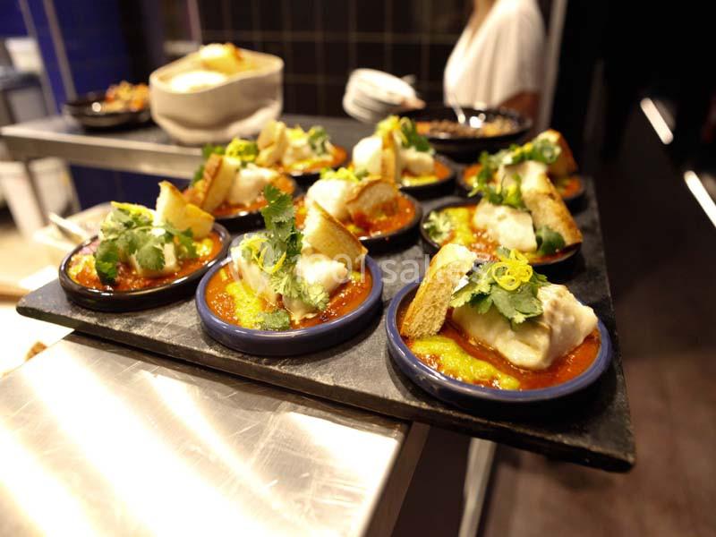 Assiettes individuelles de poisson sur sauce rouge, garnies de coriandre et de croûtons, servies sur un plateau.