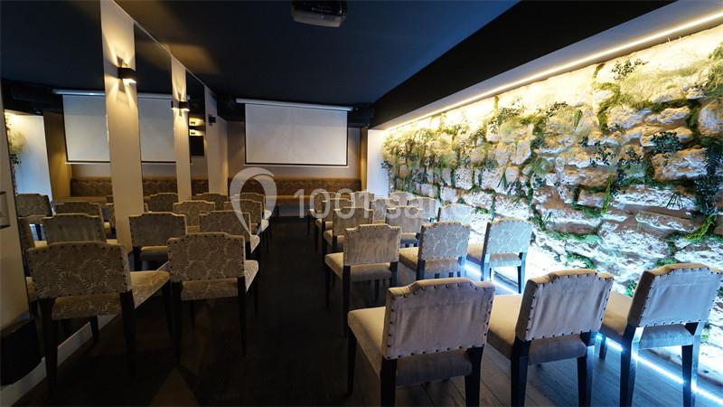 Salle de conférence avec des rangées de chaises, un mur végétalisé éclairé et deux écrans de projection.