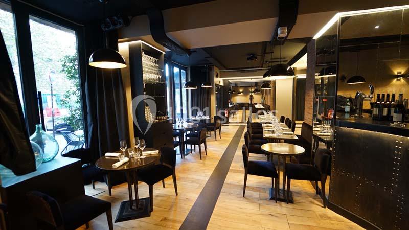 Salle de restaurant moderne avec tables dressées, éclairage tamisé et grandes baies vitrées donnant sur l'extérieur.