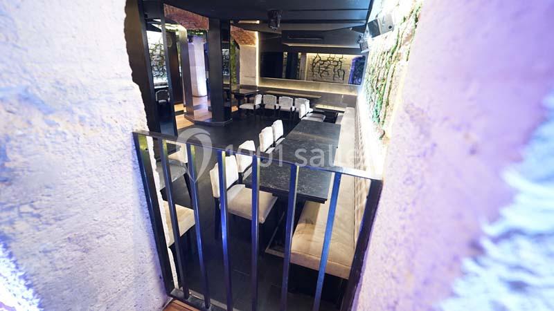 Salle moderne avec des murs en pierre, une longue table noire entourée de chaises blanches et une ambiance lumineuse tamisée.