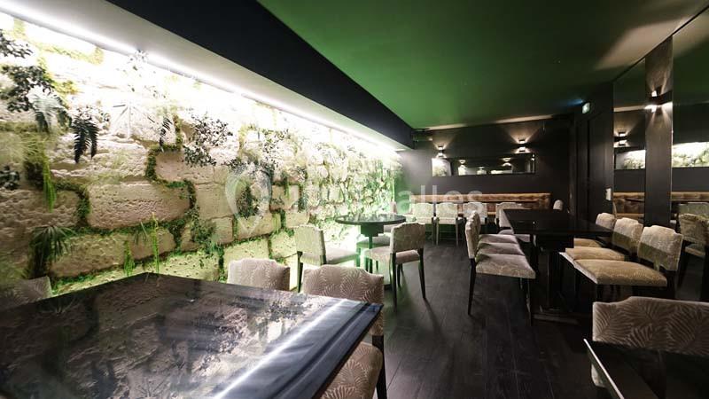 Salle de restaurant moderne avec murs végétalisés, tables en bois sombre et chaises rembourrées claires.