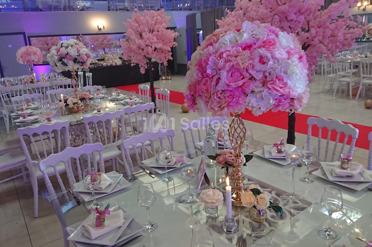 Salle de réception décorée avec des tables élégantes, des fleurs roses et des chaises blanches, ambiance festive.