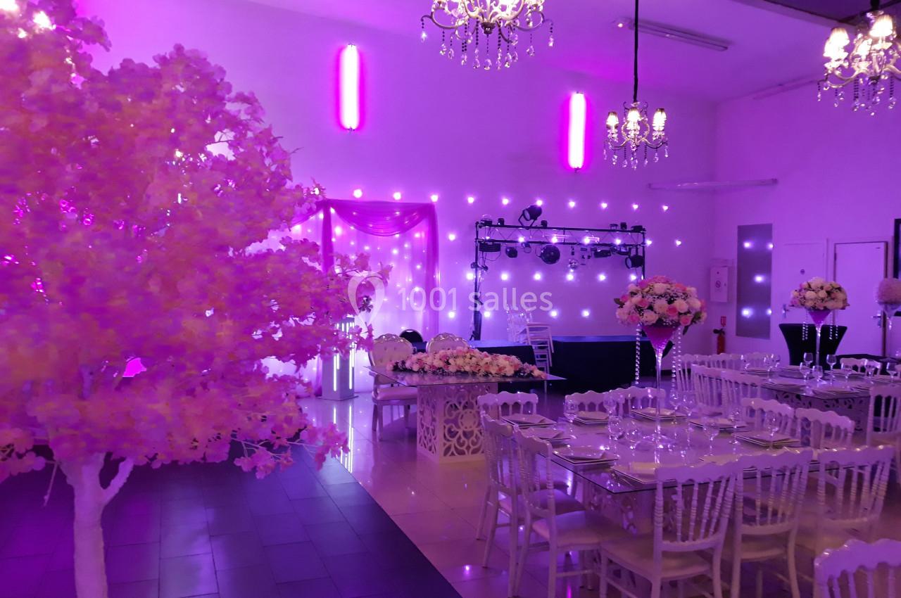 Salle de réception décorée avec des tables dressées, des fleurs et un éclairage violet tamisé.