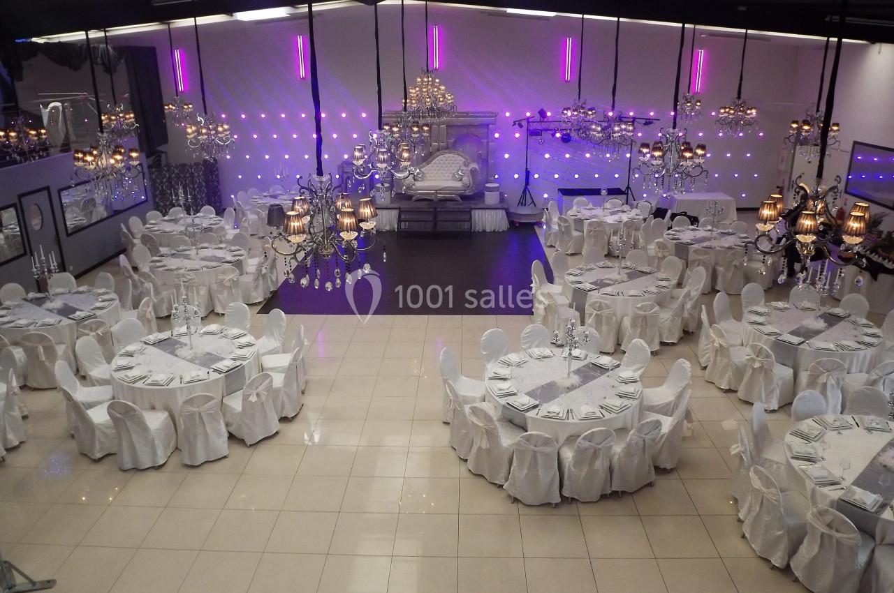 Salle de réception élégante avec tables rondes dressées, chaises blanches et éclairage décoratif violet.