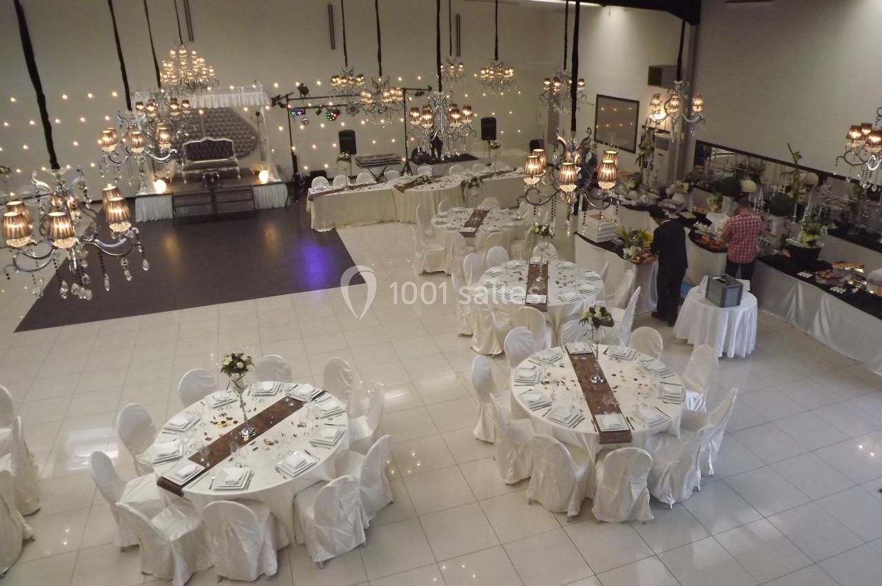 Salle de réception élégante avec tables rondes dressées, nappes blanches et buffet en arrière-plan.