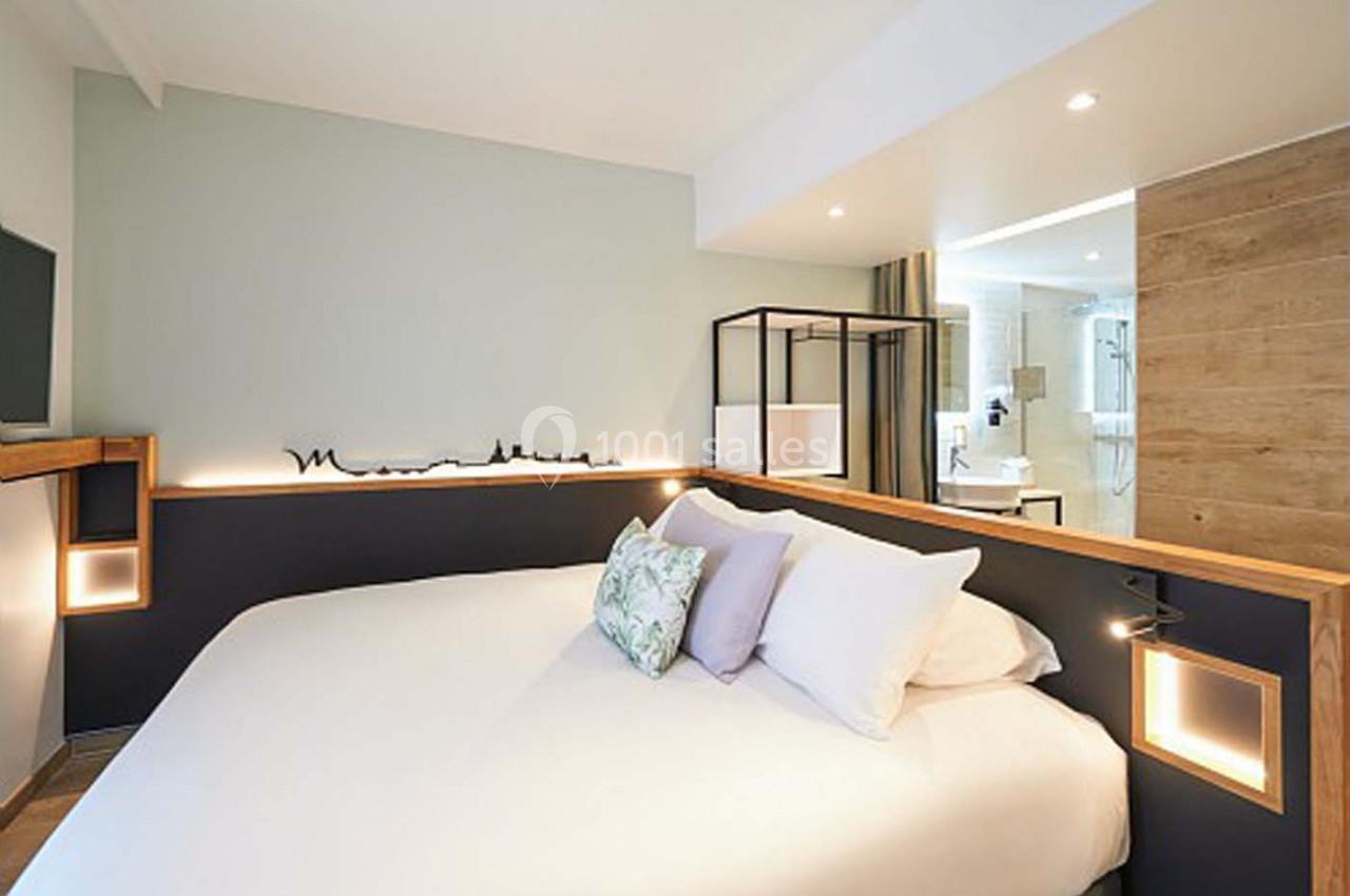 Chambre moderne avec lit double, éclairage intégré, décoration minimaliste et salle de bain visible en arrière-plan.