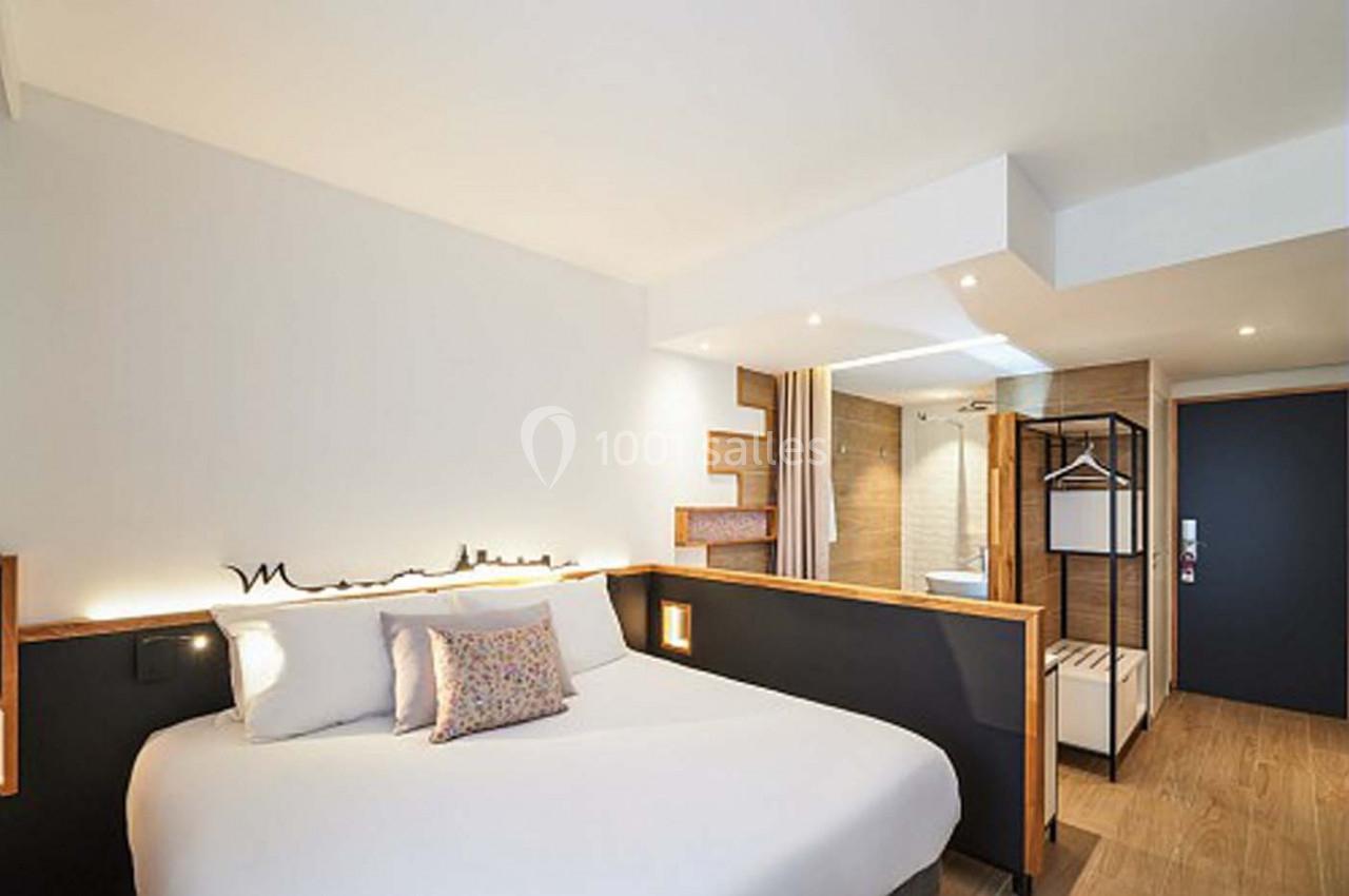 Chambre d'hôtel moderne avec lit double, décoration minimaliste, salle de bain ouverte et éclairage chaleureux.