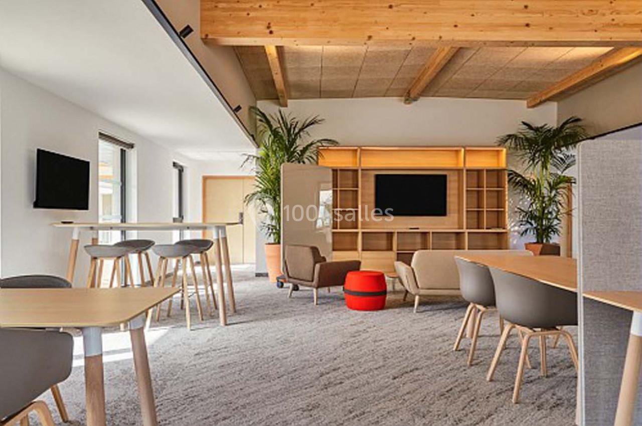 Espace de travail moderne avec tables, chaises, étagères en bois, plantes et éclairage naturel.